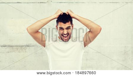 emotions, stress, madness and people concept - crazy shouting man rending ones hair in t-shirt over gray stone wall background