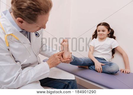 Special test. Pleasant focused capable rheumatologist running a checkup on girls reflexes while conducting a test working on her diagnosis