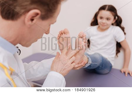 Must look the same. Precise dedicated prominent rheumatologist examining patients soles while trying figuring out the diagnosis and running a test