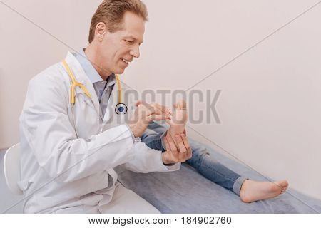 Scrupulous approach. Competent good professional doctor making a massage while treating girl who lying on a bed in his office