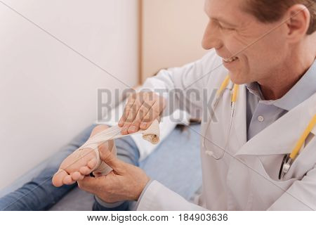 Ankle protection. Neat distinguished local rheumatologist applying elastic bondage for treating patients joints and preventing any damage