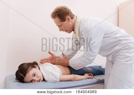 Medical methods. Capable trained gentle rheumatologist conducting special procedure while treating his little patient who lying on a bed in his office