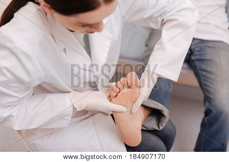 Touch for healing. Dedicated experienced trained professional massaging special spots on mans foot for relieving him from the pain in joints he experiencing