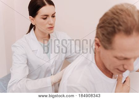 Determined medical worker. Diligent precise clever rheumatologist looking serious while checking patients spine and fulfilling her job