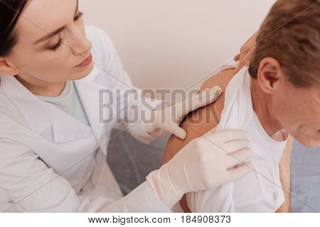 Responsibility for health. Prominent nice determined doctor asking her patient about his pain while examining his back and figuring out the diagnosis