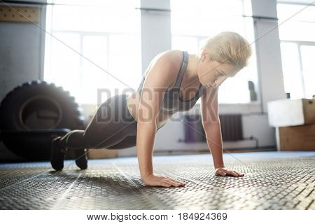Attractive young woman wrapped up in fitness training: she doing plank exercise and looking down with concentration, full-length portrait