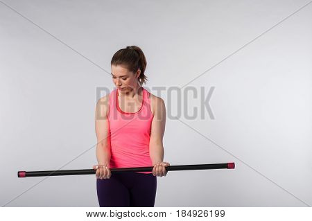 Young fit woman exercising with bodybar doing biceps exercise. Sporty girl wearing pink top posing on white background. Fitness concept.