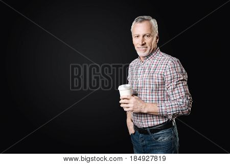 Love cappuccino. Handsome pensioner having break, putting right hand into pocket of his jeans looking straight at camera