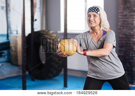 Sports activity. Delighted well built active woman holding a ball and working out with it while doing sports activities