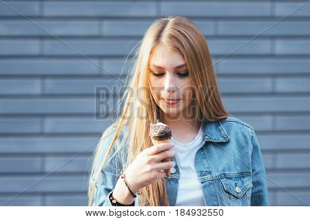 Young blonde hipster girl eating a delicious ice cream. Stylish young hipster girl eating ice cream on a blue background. Chocolate ice cream in summer