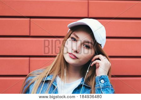 Energy girl with blue headphones listening to music with closed eyes on blue background in studio. She wears white T-shirt shorts. Long curly hair in tail is flying from moving.