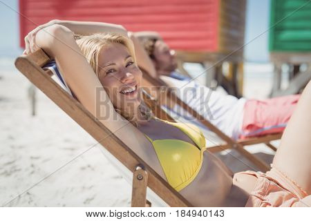 Portrait of young woman relaxaing on lounge chair at beach during sunny day