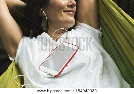 Woman using smart phone with earphone laying on hammock