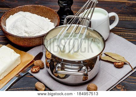 Preparation of bechamel sauce in a pan and ingredients on the wooden table