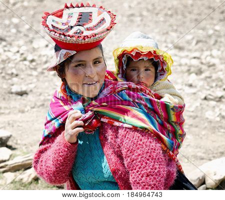 Close up portrait of a smiling Quechua woman dressed in colourful traditional handmade outfit and carrying her baby in a sling. October 21 2012 - Patachancha Cuzco Peru