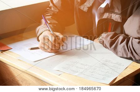 boy student testing in exercise paper exams answer sheets on wood table in classroom