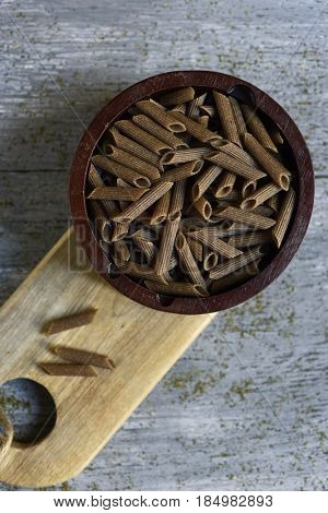 high-angle shot of a wooden bowl full of uncooked buckwheat penne rigate on a gray rustic wooden table