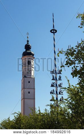 Typical Bavarian church tower and a traditional maibaum maypole against the blue sky in Dorfen Bavaria Germany