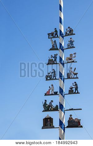 Typical Bavarian maibaum or maypole in blue and white colors with wooden figures of various professions on a sunny day against the clear blue sky with copy space in Dorfen Bavaria Germany vertical