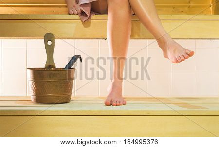 Female legs crossed in sauna. Woman sitting on the wooden bench and enjoying the hot relaxing air. Traditional Finnish relaxation and healthy lifestyle.