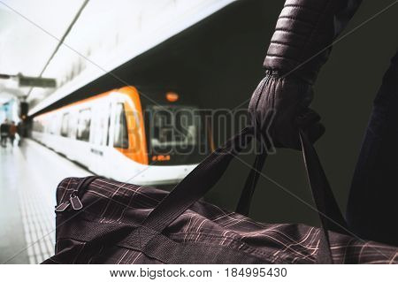 Terrorist in subway. Suspicious man standing in underground platform holding black bag. Planning a bomb attack in metro station. Train and people in background. Terrorism and security threat concept.