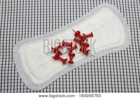 Red sharp office pins and clean menstruation cotton sanitary daily pad on the plaid cloth. Photo for woman hygiene protection. Soft tender protection woman critical days menstruation cycle