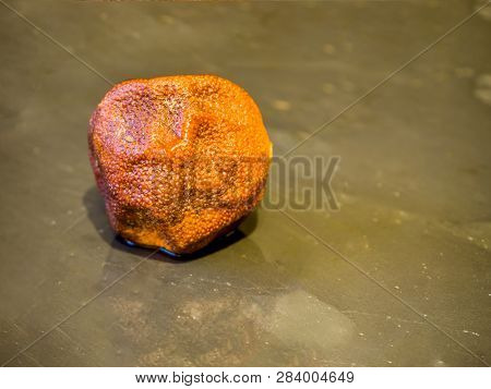 The Old Wrinkled Stale Overripe Mandarin.  Rotten Black Stone Dish Background. Top View. Free Copy S