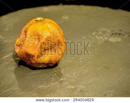 The Old Wrinkled Stale Overripe Mandarin.  Rotten Black Stone Dish Background. Top View. Free Copy S