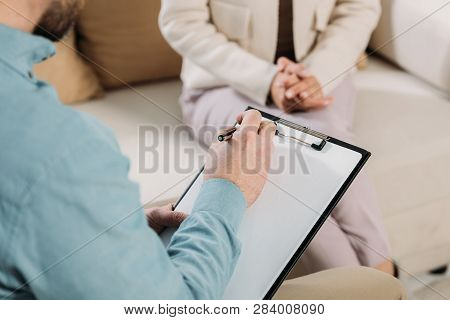 Cropped Shot Of Psychotherapist Writing On Clipboard And Female Patient Sitting On Couch