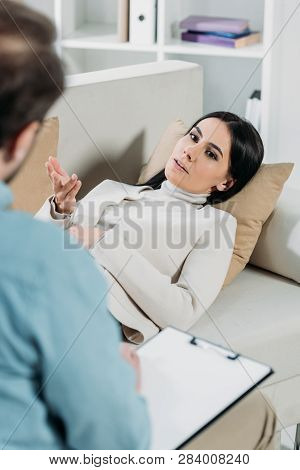 Young Woman Lying On Couch And Talking With Professional Psychotherapist