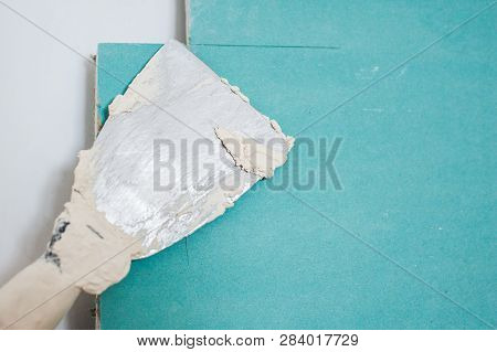 Spatula With Putty. The Process Of Applying The Paste On The Blue Gypsum. Repair Work, Decoration Bu