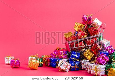Small Shopping Cart With Presents On Pink Background. Trolley From A Supermarket Full Of Colorful Gi