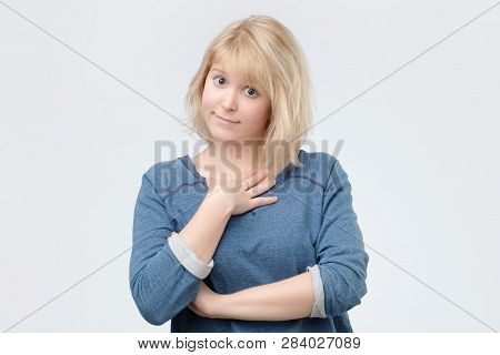 Woman With Blonde Dyed Hair Wearing Blue Pulover Smiling Broadly And Keeping Hand On Her Cheek