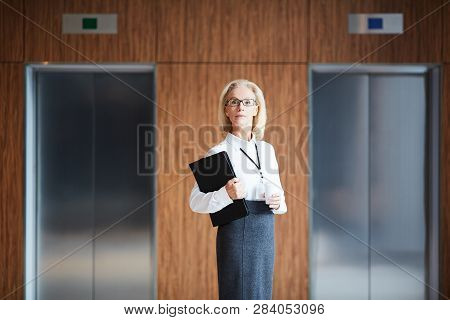 Confident Blonde Businesswoman With Documents And Drink Standing Between Elevator Doors Inside Moder
