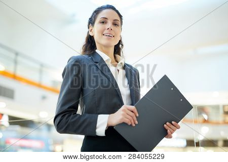 Young Successful Secretary Or Economist With Clipboard Standing In Front Of Camera
