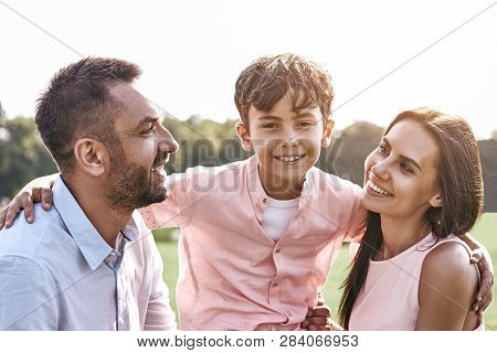 Bonding. Family Of Three Walking On Grassy Field Son Hugging Par