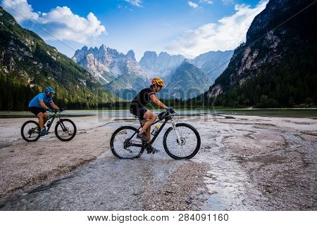 Tourist cycling in Cortina d'Ampezzo, stunning rocky mountains on the background. Family riding MTB enduro flow trail. South Tyrol province of Italy, Dolomites.
