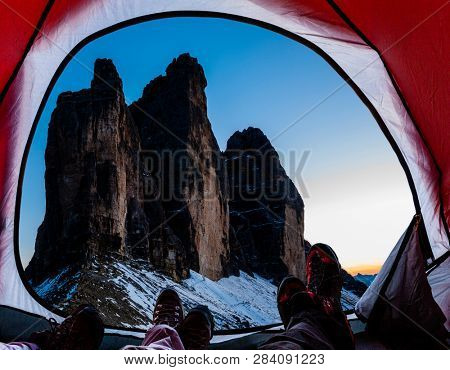 Night bivouac at Tre Cime di Lavaredo, milion star hotel under night sky, red illuminated tent on pass in Dolomites, Italy.