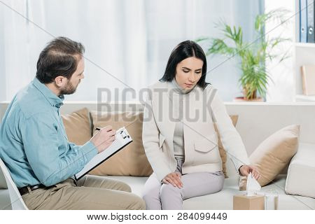 Upset Young Woman Holding Paper Tissue During Therapy Session With Psychiatrist