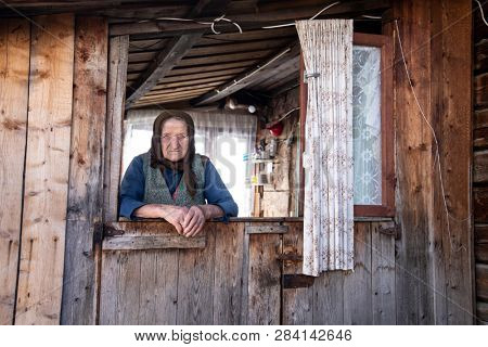 Muntele Bocului, Romania - February 7, 2019: Old rural woman called Lele Maria standing in the porch