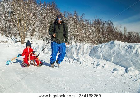 Happy Father And His Son Enjoying Sledding Ride. Happy Family With Sled In Winter Having Fun Togethe