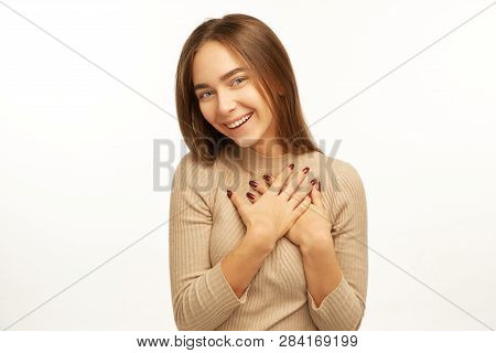 Happy Cute Young Woman Folds Arms On Chest, Expresses Gratitude, Has Tender Smile Isolated Over Whit