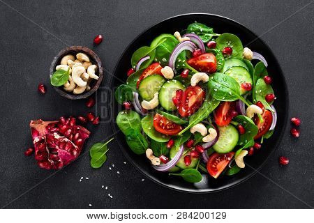 Spinach Salad With Fresh Cucumbers, Tomato, Onion, Pomegranate, Sesame Seeds And Cashew Nuts On Blac