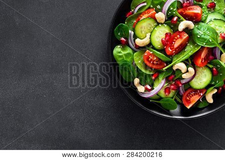 Spinach Salad With Fresh Cucumbers, Tomato, Onion, Pomegranate, Sesame Seeds And Cashew Nuts On Blac