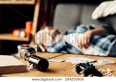 Selective Focus Of Bottle Lying On Coffee Table With Man Sleeping With Bra On Face On Background