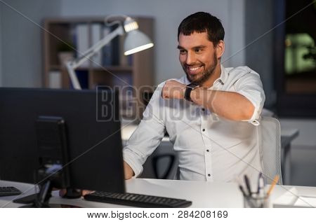 business, technology and time management concept - happy businessman using voice command recorder on smart watch at nigh office