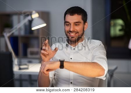 business, technology and time management concept - happy smiling businessman using gestures with smartwatch at nigh office