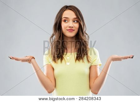 choice and people concept - smiling young woman or teenage girl in blank yellow t-shirt holding something imaginary over grey background