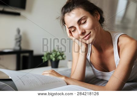 Beautiful young woman realxing on a couch at home, reading, eating green apple