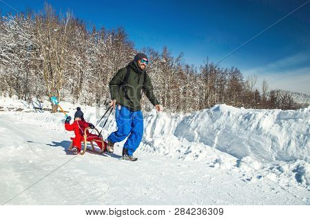 Happy Father And His Son Enjoying Sledding Ride. Happy Family With Sled In Winter Having Fun Togethe